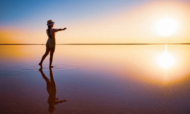 Bir kız ellerini tuz gölünün ayna yüzeyindeki batan güneşe uzatır.