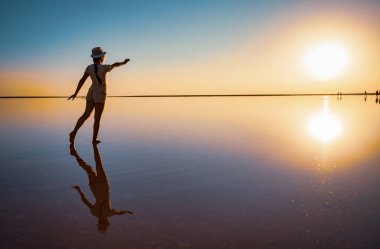 Bir kız ellerini tuz gölünün ayna yüzeyindeki batan güneşe uzatır.