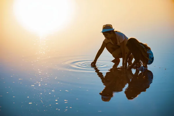 Duas meninas em um belo lago transparente estão à procura de algo em uma superfície brilhante — Fotografia de Stock