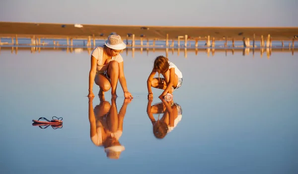 Two fantastically beautiful girls on a beautiful transparent lake are looking for something in a shiny surface — Stock Photo, Image