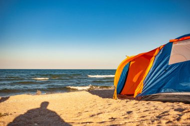 Güzel, ışıl ışıl bir denizin kıyısında büyük bir kamp çadırı duruyor.