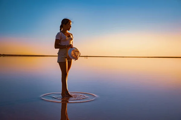 Happy girl walks along the mirror lake enjoying the evening sun views of the fiery sunset — Stock Photo, Image