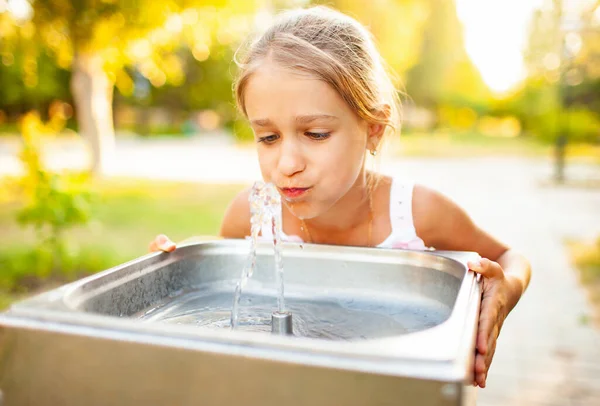 Fröhliches wunderbares Mädchen trinkt frisches Wasser aus einem kleinen Brunnen in einem sommerlich warmen, sonnigen Park — Stockfoto