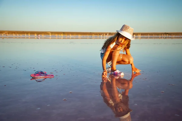 Uma menina bonita está olhando para algo em uma superfície de água transparente em um fundo transparente — Fotografia de Stock