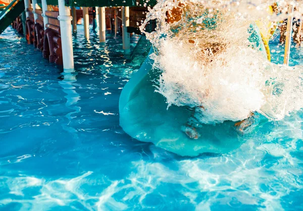 Uma criança alegre desce de um brilhante túnel deslizante para a piscina e faz salpicos — Fotografia de Stock