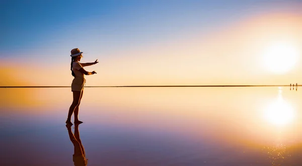 A girl reaches out with her hands to the setting sun on the mirror surface of a salt lake — Stock Photo, Image