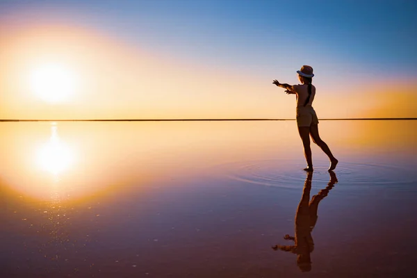 O fată ajunge cu mâinile la apusul soarelui pe suprafața oglinzii unui lac de sare — Fotografie, imagine de stoc