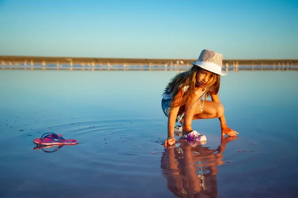 Uma menina bonita está olhando para algo em uma superfície de água transparente em um fundo transparente — Fotografia de Stock