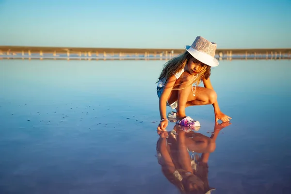 Uma menina bonita está olhando para algo em uma superfície de água transparente em um fundo transparente — Fotografia de Stock