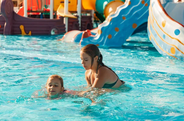 La hermana ayuda a aprender a nadar en la piscina con agua clara y transparente — Foto de Stock