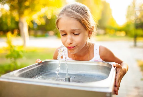 Fröhliches wunderbares Mädchen trinkt frisches Wasser aus einem kleinen Brunnen in einem sommerlich warmen, sonnigen Park — Stockfoto