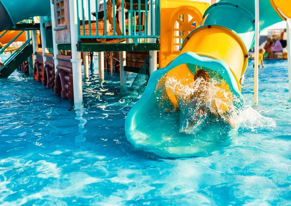 Un niño alegre desciende de un túnel de deslizamiento brillante a la piscina y hace salpicaduras — Foto de Stock