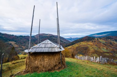 Yeşil bir çayırda yağmurdan alınan bir filmle kaplı büyük bir saman yığını. Hava bulutlu değil.