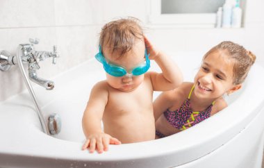 Yüzme gözlüklü komik çocuk banyoda kız kardeşinin yanında duruyor.