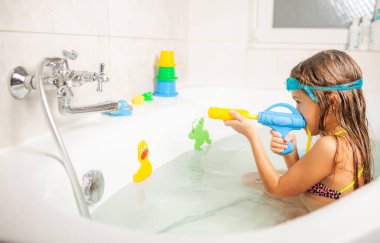 Su bardaklı komik küçük kız banyoda otururken su tabancasıyla oynanıyor.