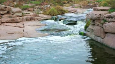 Pürüzsüz ve karanlık taşların arasında küçük parlak bir dere akıyor.