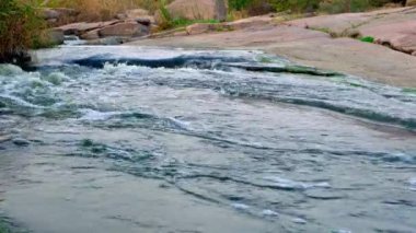 Pürüzsüz ve karanlık taşların arasında küçük parlak bir dere akıyor.