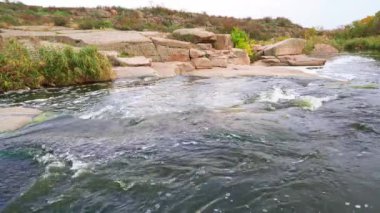 Pürüzsüz ve karanlık taşların arasında küçük parlak bir dere akıyor.