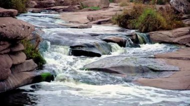 Pürüzsüz ve karanlık taşların arasında küçük parlak bir dere akıyor.