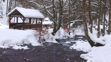 Ormanın derinliklerinde bir dağ deresinin yanında ahşap bir taraça ve insanlar vadiden tırmanarak yanından geçiyorlar.