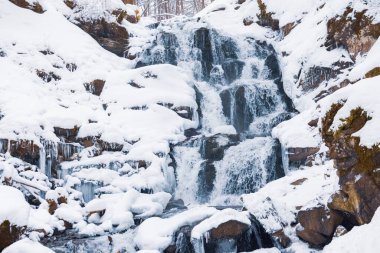 Soğuk su şelalesi karla kaplı taşlar arasında akıyor.