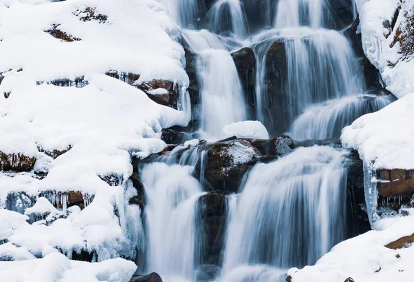 Petite cascade d'eau froide coulant parmi les pierres recouvertes de neige — Photo