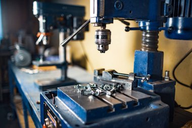 Metal krom cıvatalar ve fındıklar iş yerindeki sondaj makinesinde yatıyor.