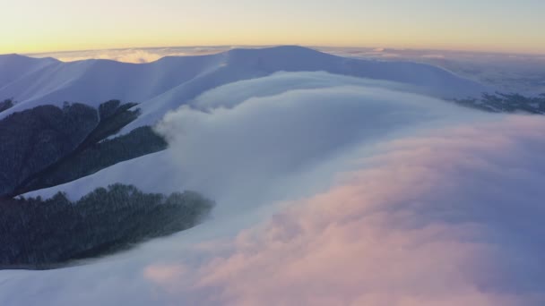 Ondas de nuvens fluem suavemente e lentamente sobre os topos de montanhas cobertas de neve cobertas com florestas de abeto em um pôr do sol frio — Vídeo de Stock