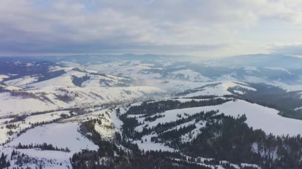 Malá zasněžená vesnička v obrovském horském údolí se smrkovými lesy na pozadí zamračené modré oblohy — Stock video