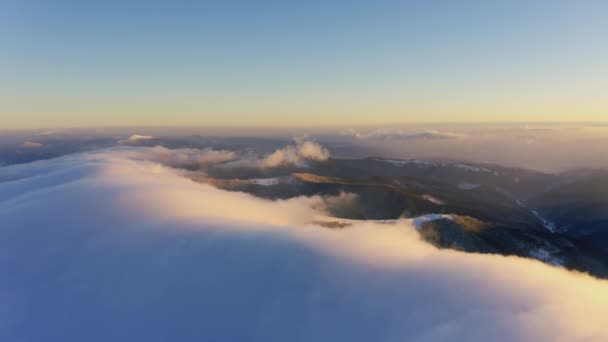 Las olas de nubes fluyen suave y lentamente sobre las cumbres de las montañas cubiertas de nieve cubiertas de bosques de abetos en una fría puesta de sol. — Vídeo de stock