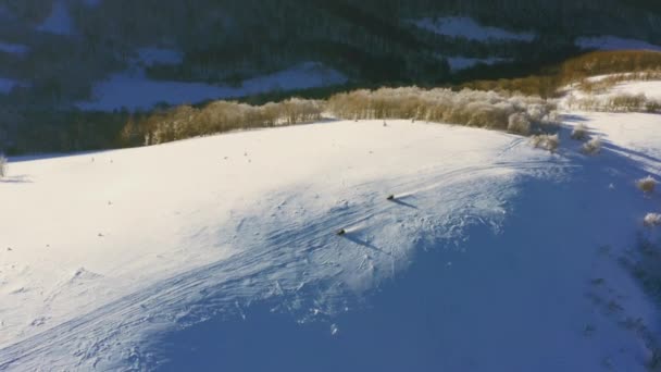 Een snelle man op een sneeuwscooter rijdt een verlaten helling van een besneeuwde berg bij een heldere zonsondergang — Stockvideo