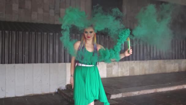 Jolie fille dans une robe verte avec des tresses africaines et un maquillage coloré posant avec de la fumée vert vif dans les rues — Video