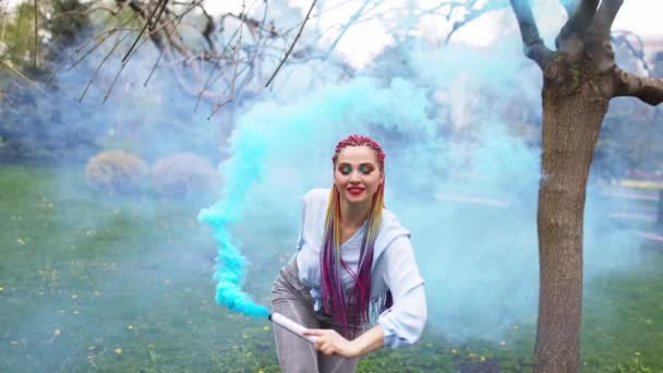 Belle fille avec des tresses africaines multicolores posant avec de la fumée bleue sur le fond du parc vert — Video