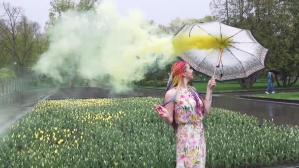 Menina com tranças africanas e maquiagem em vestido de primavera está dançando na chuva com guarda-chuva em fumaça amarela em um parque da cidade — Vídeo de Stock