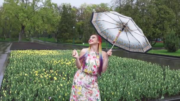 Chica con trenzas africanas y maquillaje en vestido de primavera está bailando bajo la lluvia con paraguas en humo amarillo en un parque de la ciudad — Vídeo de stock