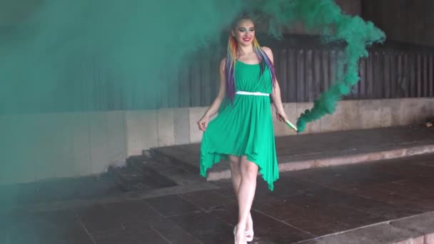 Cute girl w zielonej sukience z afrykańskich warkoczach i kolorowy makijaż pozowanie z jasnym zielonym dymem na ulicach — Wideo stockowe