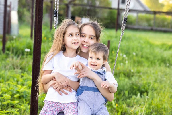 Crianças alegres em roupas leves montam um balanço de rua em um jardim de casa verde florescente e riem em um sorriso feliz — Fotografia de Stock