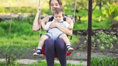 Şirin abiler ve ablalar, ılık bir bahar gününde yeşil çiçek açan bir bahçenin zemininde parlak bir salıncakta gezerler.