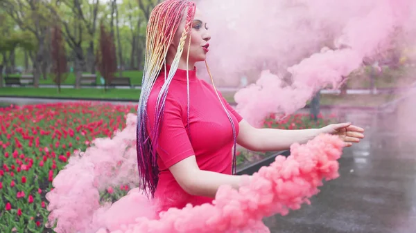 Een meisje met make-up met regenboog vlechten in rode jurk poseren in re — Stockfoto