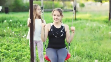 Hafif giysili neşeli çocuklar yeşil bir bahçede salıncakta sallanıyor ve mutlu bir gülümsemeyle gülüyorlar.