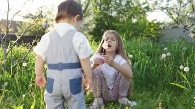 Erkek ve kız kardeş, ılık bir bahar bahçesinde çiçek açan beyaz sarı ve tüylü karahindibalarla oynarken eğleniyorlar.