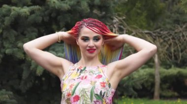 Afrika örgülü ve makyajlı bir elbiseyle gülümseyen ve saçlarını bahar yağmurlu parkında toplayan bir kız.