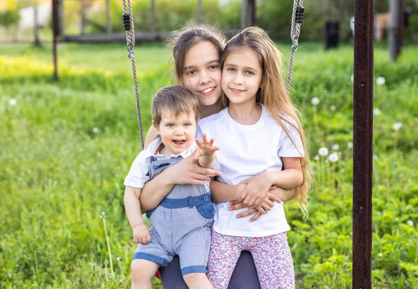 Crianças alegres em roupas leves montam um balanço de rua em um jardim de casa verde florescente e riem em um sorriso feliz — Fotografia de Stock