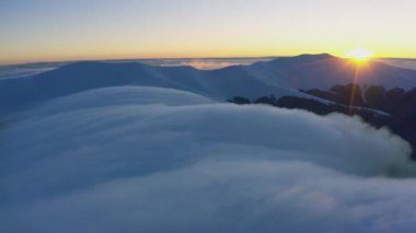 Bulut dalgaları yavaşça kar kaplı dağların tepelerinden akar. Soğuk bir günbatımında ladin ormanlarıyla kaplıdır.