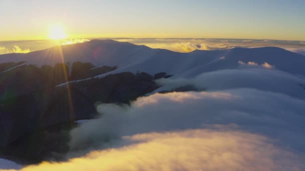 Хмарні хвилі м'яко і повільно течуть над вершинами засніжених гір, вкритих ялиновими лісами на холодному заході сонця — стокове відео