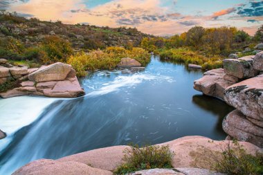 Nehir, altın sonbaharda çimlerle kaplı beyaz ıslak taşların arasında akar.