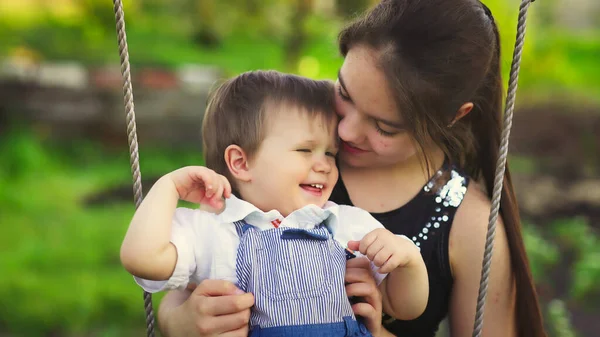 Frate drăguț și sora mai mare plimbare pe un leagăn luminos în ziua de primăvară caldă pe fundalul unei grădini verzi înfloritoare — Fotografie, imagine de stoc