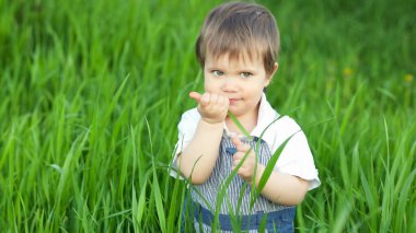 Tulum giymiş mavi parlak gözlü, kocaman bir bahçede taze yeşil çimen yiyen komik küçük çocuk.