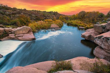 Pürüzsüz, ıslak ve karanlık taşların ve kuru alçak ağaçların arasında küçük, parlak bir dere akıyor.