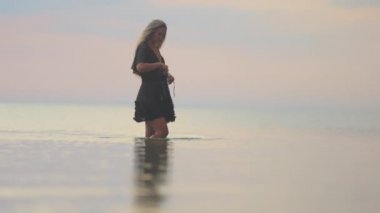 Siyah bikinili, sarı şık saçlı ve dantel şallı bir kız nehir boyunca yürüyor.